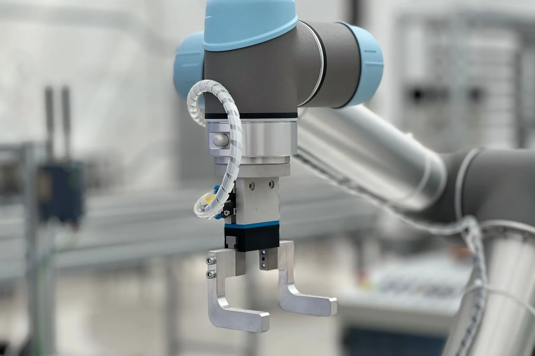A collaborative robot gripper in close up, with the production line blurred behind it