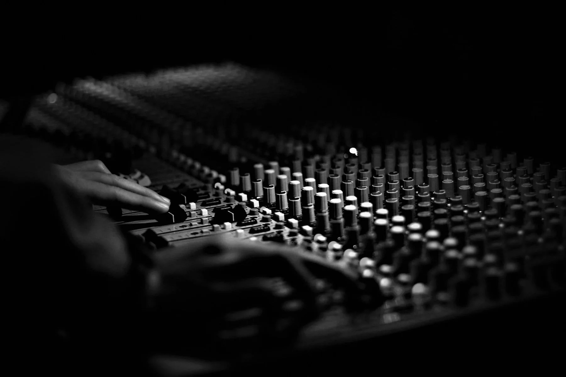 A recording engineer working the faders of a mixing console, photographed in black and white