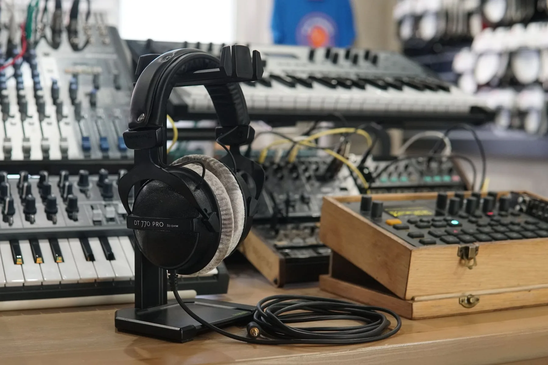 Studio headphones resting on a stand in front of outboard audio equipment and a mixing desk