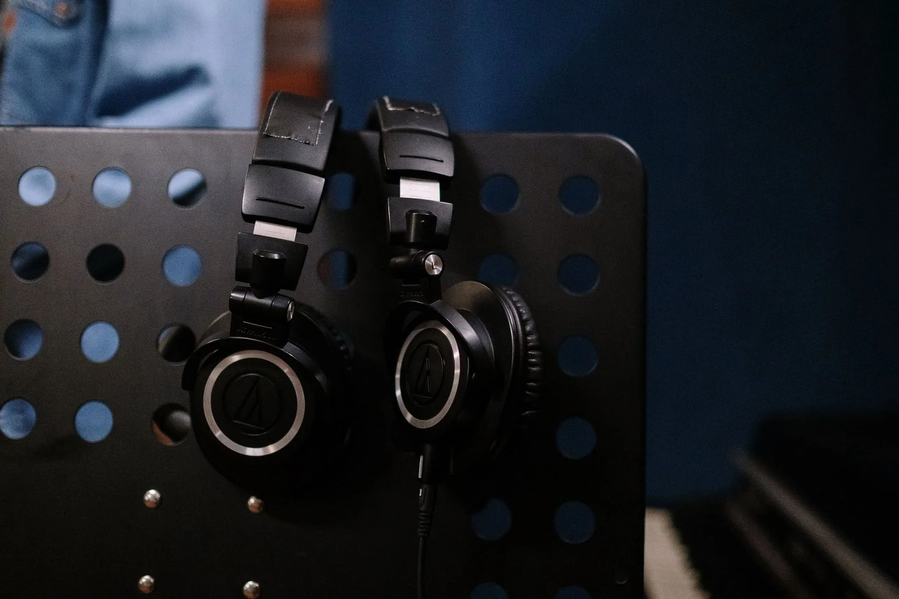 Two pairs of studio headphones hanging on a perforated metal stand