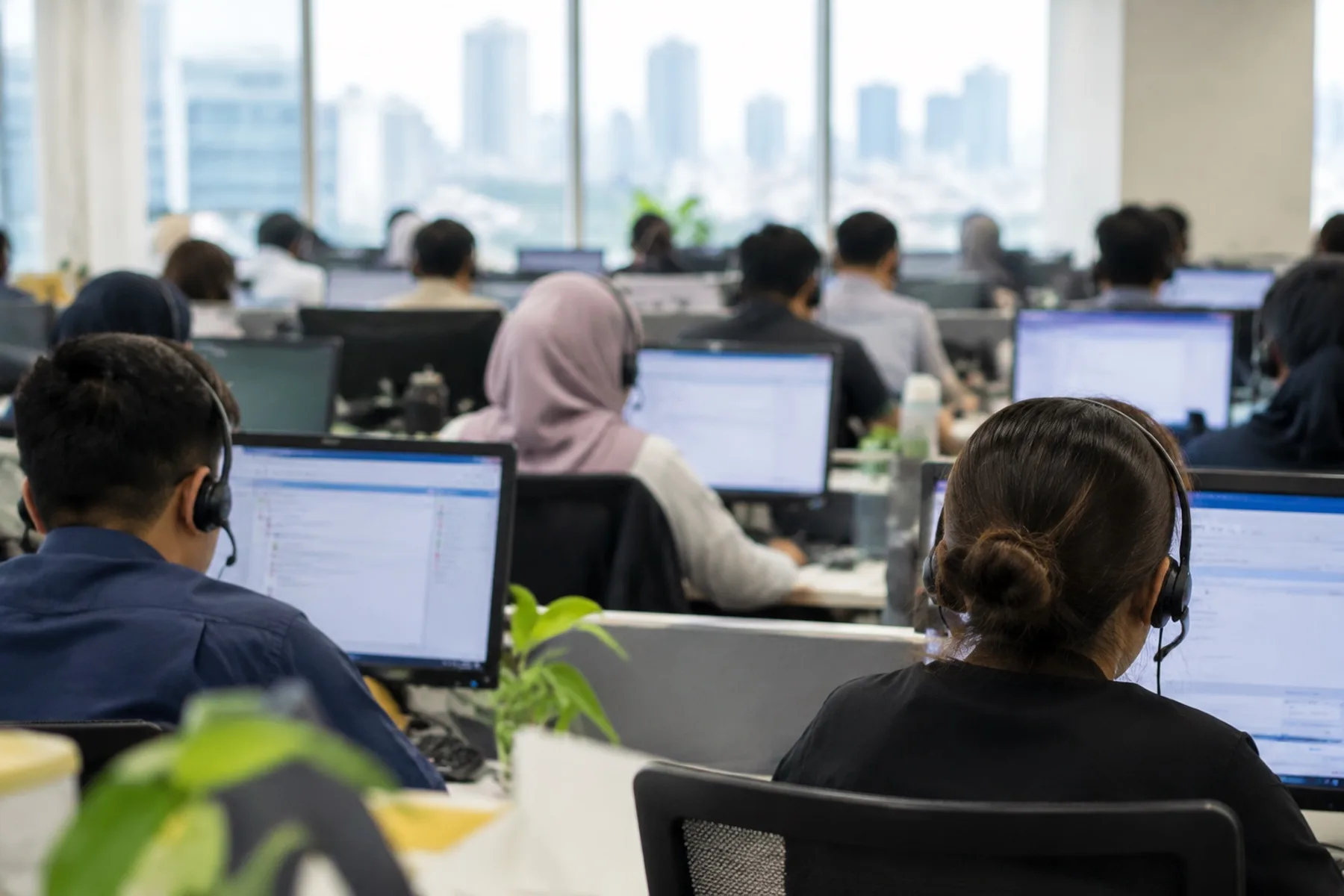 Rows of call center agents wearing headsets, seen from behind in soft focus