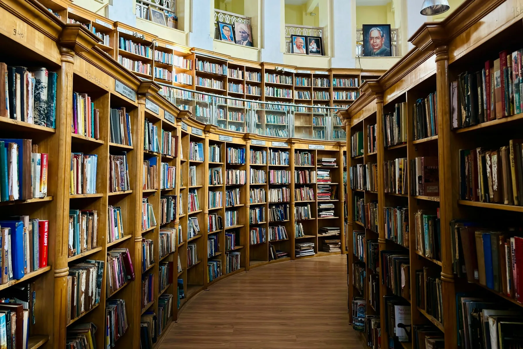 A wooden shelf of books beside framed portraits