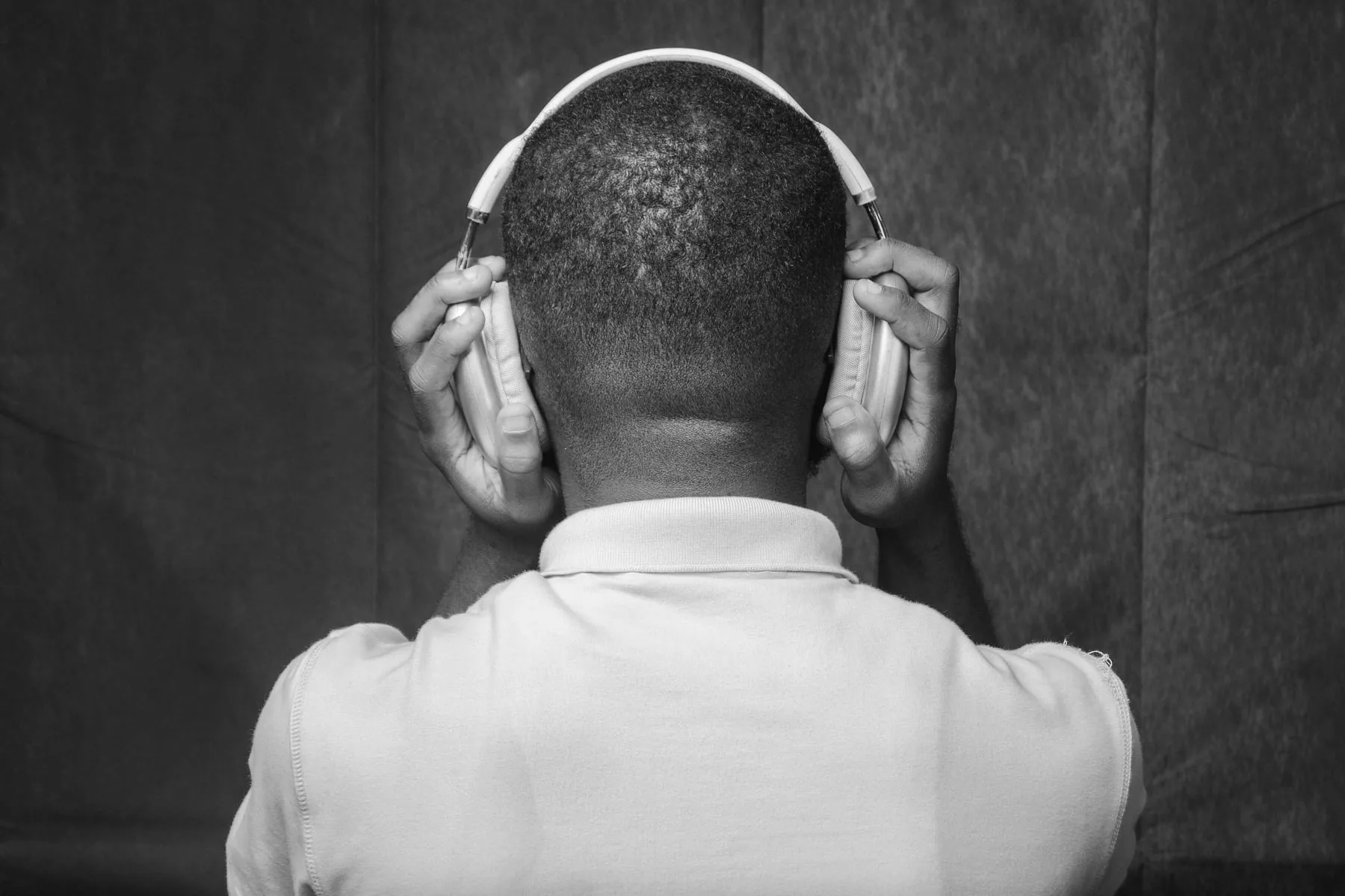 A person seen from behind pressing both hands against their headphones, in black and white