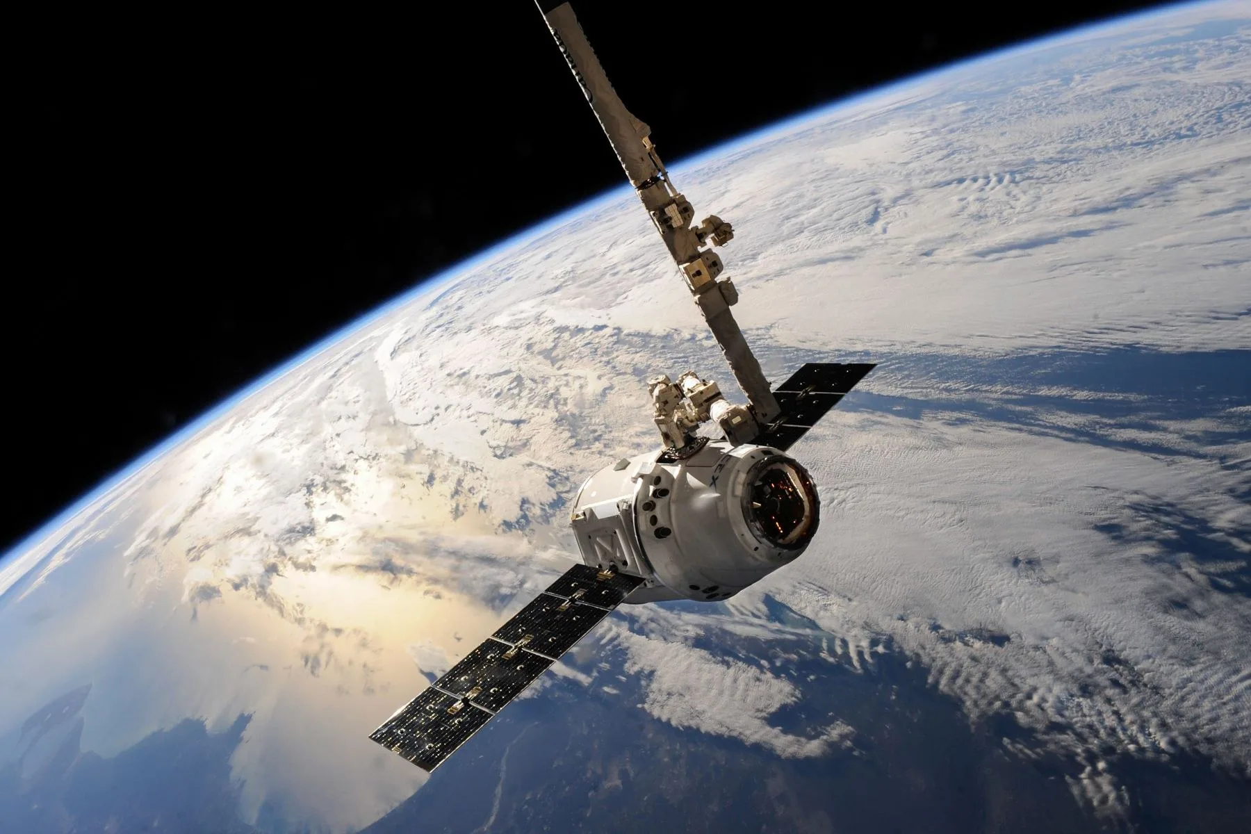 A satellite in orbit with the curved surface of the Earth and cloud cover below