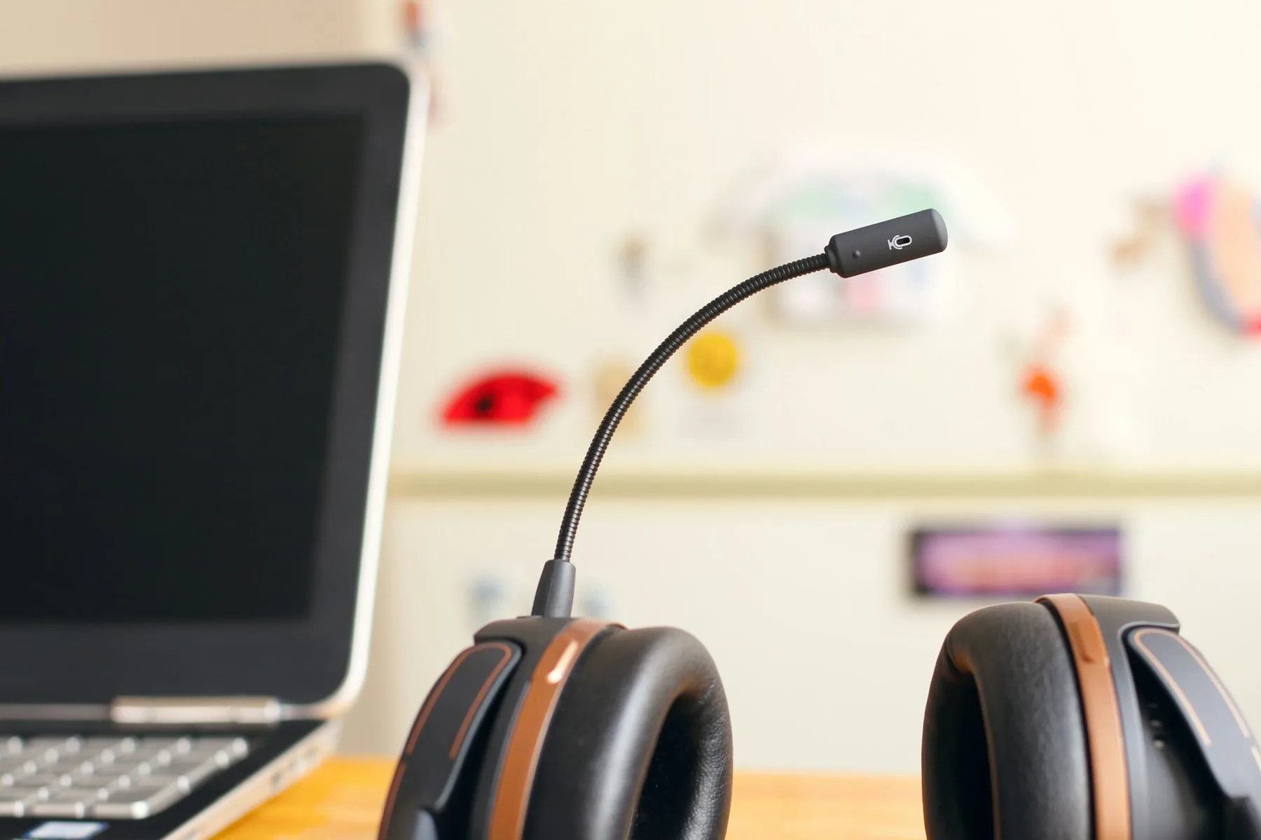 A black and copper headset with a boom microphone resting on a wooden desk beside an open laptop