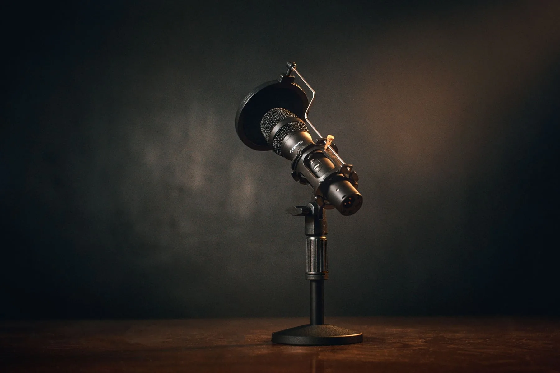 A microphone on a desk stand lit by a single warm light in a dark room