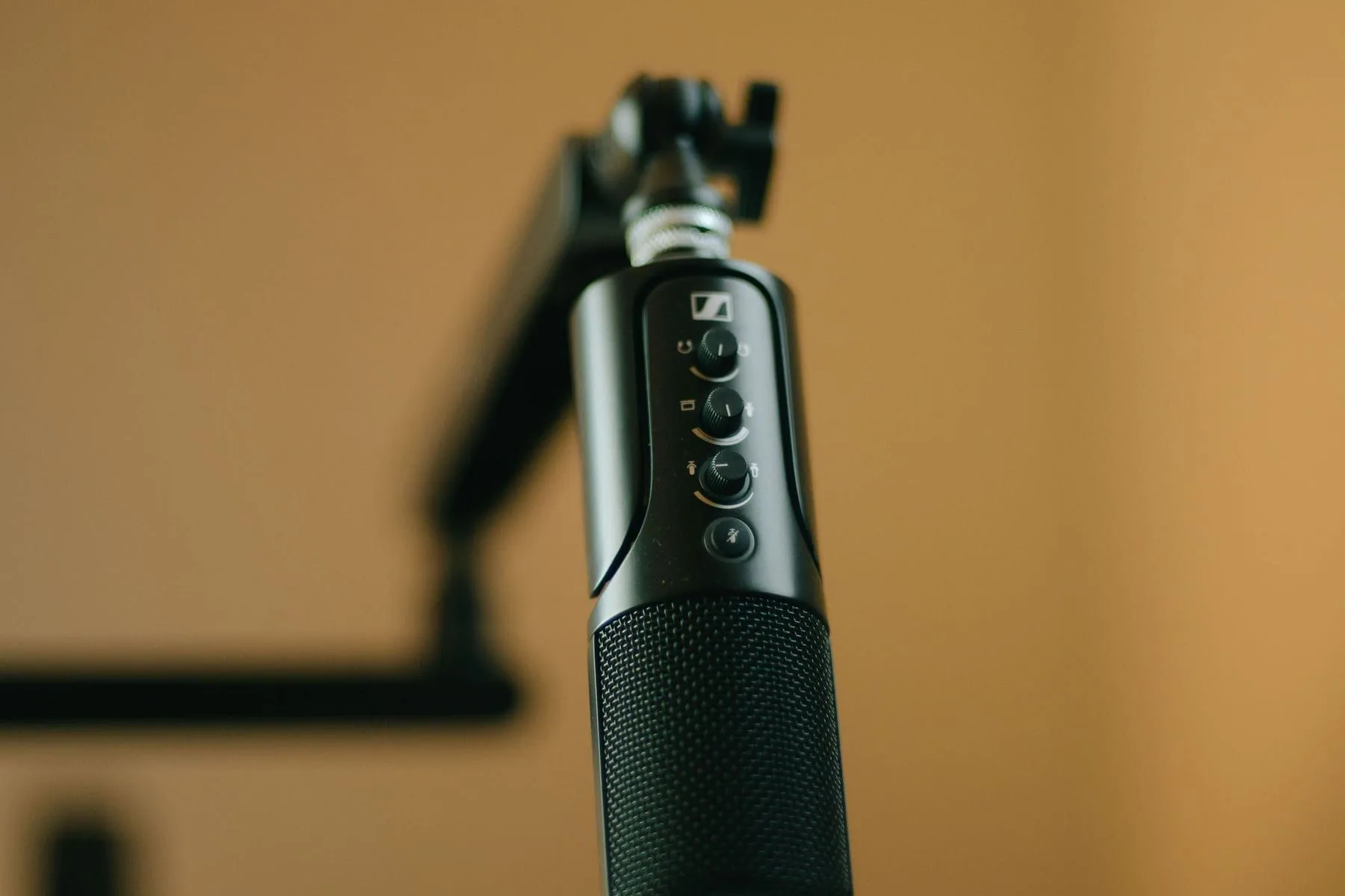 A broadcast microphone on a boom arm against a warm yellow background
